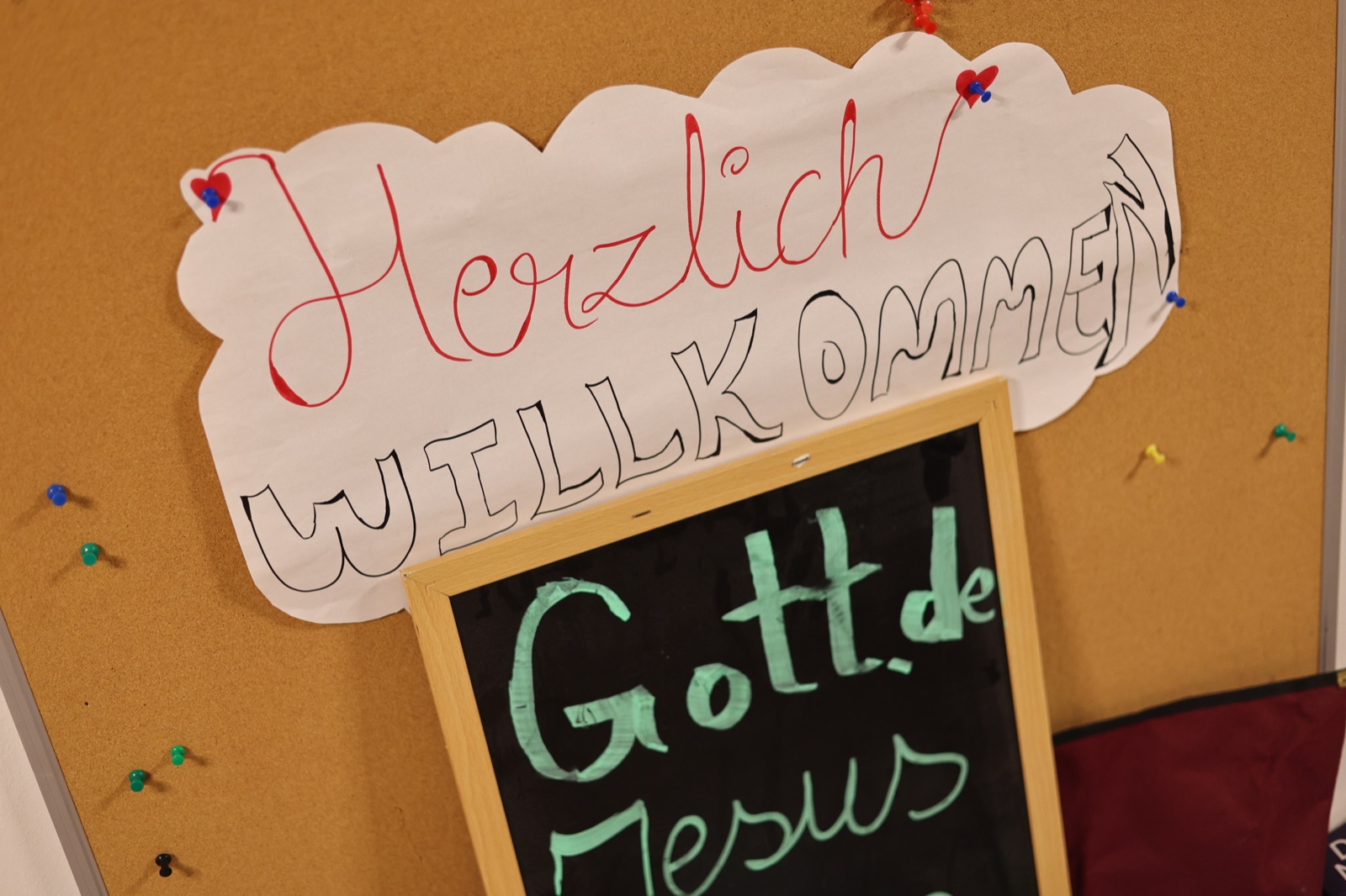 Ein handgemachtes Willkommen-Schild hängt an einer Pinnwand.